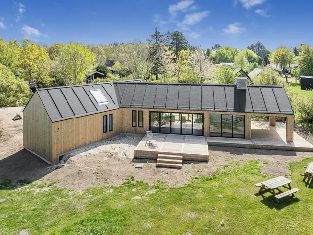 Langt sommerhus i lærk med glaspartier og terrasse set fra luften — billede 16 af 21
